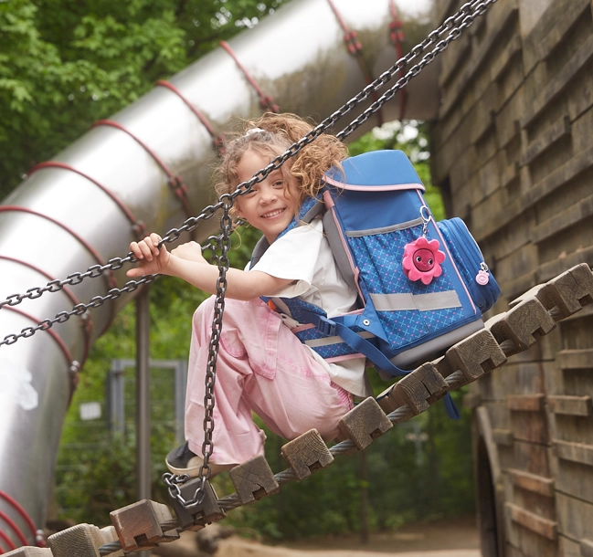 Kind sitzt auf Spielplatz auf einer Brücke und hat einen Schulranzen auf