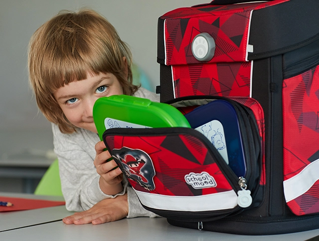 Kind holt seine Brotdose aus der Fronttasche seines Schulranzens