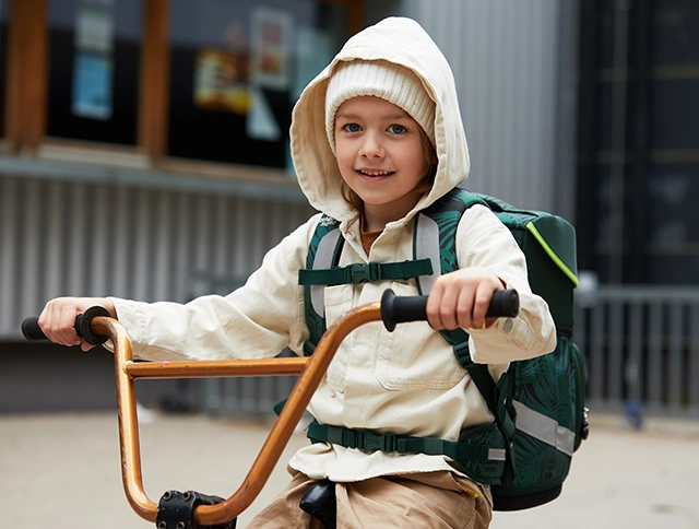 Kind mit Schulranzen auf dem Rücken sitzt auf einem Fahrrad