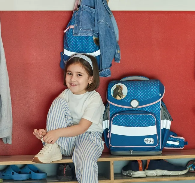 Kind bindet sich auf einer Bank den Schuuh zu und hat neben sich auf der Bank einen Schulranzen stehen