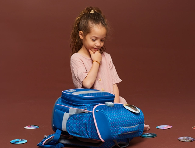 Kind sitzt nachdenklich vor einem Schulranzen und Patchies, die auf dem Boden liegen