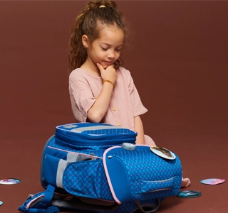 Kind sitzt nachdenklich auf dem Boden und hat einen Schulranzen vor sich liegen