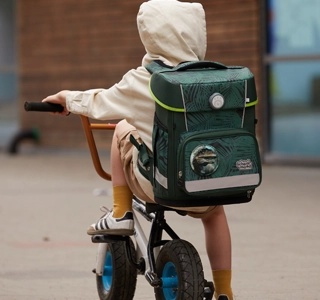 Kind sitzt auf Fahrrad und hat eine Kapuze und einen Schulranzen auf