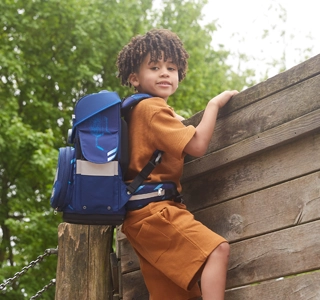 Kind mit Schulranzen auf dem Rücken klettert Holzwand hoch