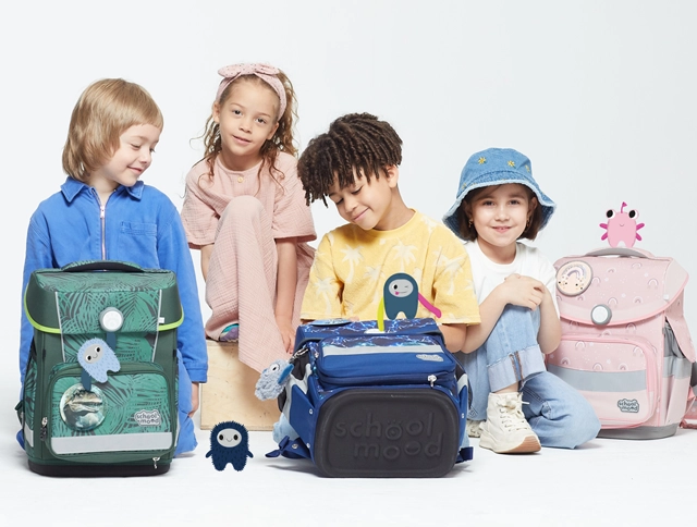 Vier Kinder sitzen auf dem Boden mit Schulranzen und Moodies